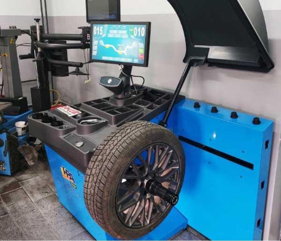 Tire balancing machine in a workshop with a mounted wheel and a screen displaying digital readings.