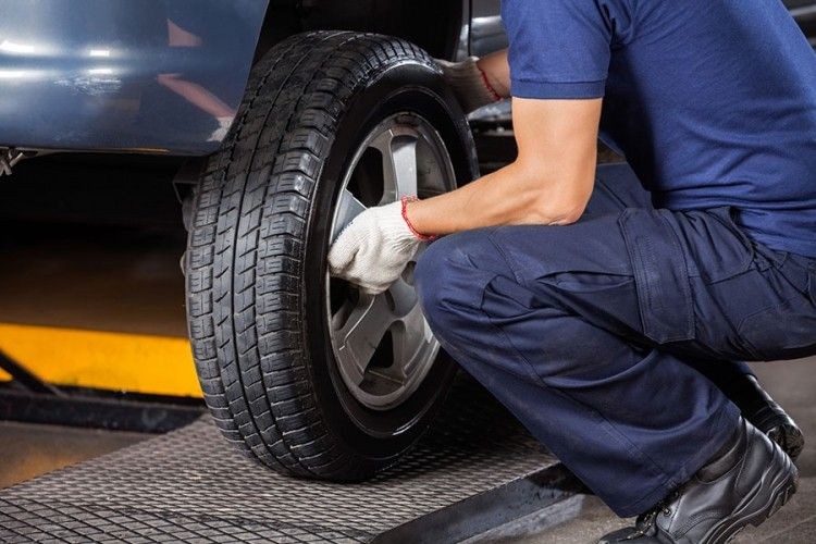 Mechanic in blue uniform changing a car tire in a garage.